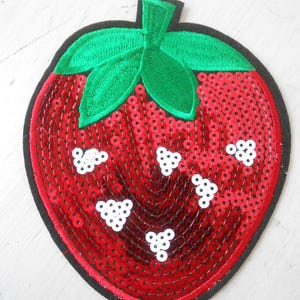 May include: A red sequined strawberry patch with a black border. The strawberry has white seed clusters and green embroidered leaves. This decorative patch can be ironed on or sewn onto clothing or accessories.