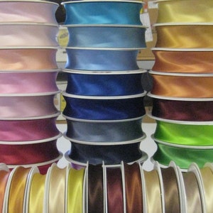 Könnte beinhalten: Sortiment von Satinbandspulen in verschiedenen Farben, darunter Rosa, Blau, Grün, Gold und Braun. Das Band ist um weiße Spulen gewickelt.