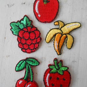 Peut inclure: Six patchs brodés thermocollants représentant différents fruits : une pomme rouge, une framboise rouge, une banane jaune, une cerise rouge et une fraise rouge.