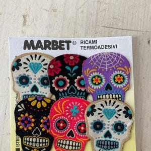 May include: A pack of six embroidered skull patches in various colours. Each skull features intricate floral and geometric designs, with a prominent diamond shape. The brand name "MARBET" is printed at the top.