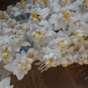 May include: A bunch of white fabric flowers with yellow centres. The flowers are arranged in a cluster and have a delicate, feminine appearance.