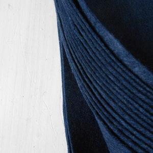 Pode incluir: Um close-up de um tecido azul escuro dobrado em uma série de pregas. O tecido é liso e tem um brilho sutil.