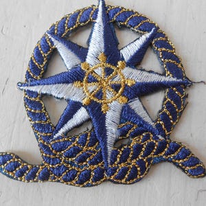May include: A blue and white embroidered patch with a gold compass and rope design.