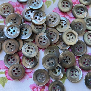 Puede incluir: Un conjunto de botones redondos grises iridiscentes, cada uno con cuatro agujeros. Los botones están dispuestos sobre un fondo floral. Estos botones son adecuados para coser y manualidades. Cada botón mide aproximadamente 2,5 cm de diámetro.