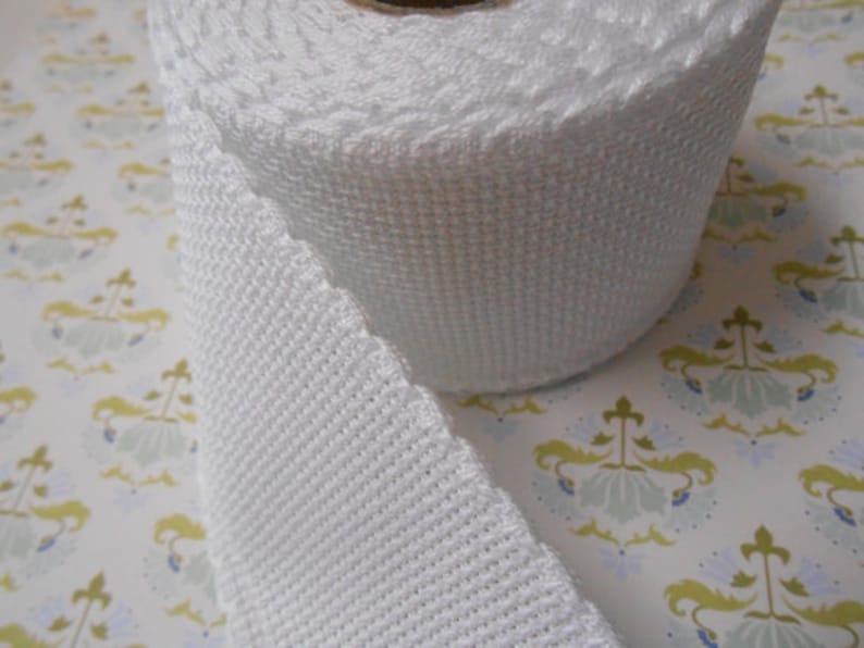May include: White cotton webbing ribbon, rolled up on a white background. The ribbon is woven with a textured pattern.