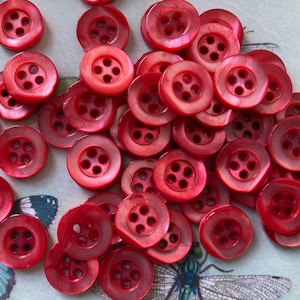 Könnte beinhalten: Ein Haufen roter, vierlöchriger Plastikknöpfe. Die Knöpfe haben eine Perlmutt-Oberfläche.