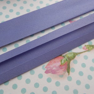May include: Two pieces of lavender purple satin ribbon, one folded over the other. The ribbon is on a white background with aqua blue polka dots.