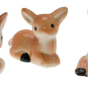 Puede incluir: Tres figuritas de cerámica de cervatillo, cada una con pelaje marrón y blanco moteado, tumbadas con la cabeza girada hacia un lado.