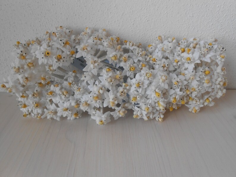 May include: A bunch of white artificial flowers with yellow centres. The flowers are arranged in a cluster and have a delicate, realistic appearance.