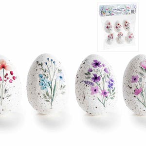 Puede incluir: Cuatro huevos de Pascua decorativos blancos moteados, cada uno adornado con un diseño floral de acuarela diferente en tonos rosa, morado y azul. Un paquete de seis huevos similares es visible en el fondo.