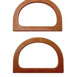 Puede incluir: Dos asas de bolso semicirculares de madera. Las asas son de color marrón cálido y tienen una forma suave y redondeada. Están diseñadas para sujetarse a un bolso, proporcionando un agarre resistente y elegante. Las asas están hechas de un material duradero.