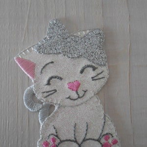 Può includere: Un gatto bianco scintillante con orecchie, naso e cuscinetti rosa. Il gatto è seduto con la coda arrotolata intorno alle zampe.