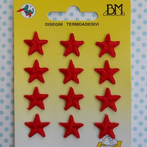 Puede incluir: Un paquete de doce parches termoadhesivos rojos en forma de estrella. Los parches están dispuestos en tres filas de cuatro sobre una tarjeta de respaldo amarilla y blanca. La tarjeta tiene el texto "DISEGNI TERMOADESIVI" y un logotipo con un dragón.