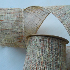 Puede incluir: Un rollo de cinta decorativa con textura tejida. La cinta es principalmente beige con toques de naranja, verde y negro. La cinta está desenrollada, revelando su textura y variaciones de color. La bobina es visible en la parte inferior.