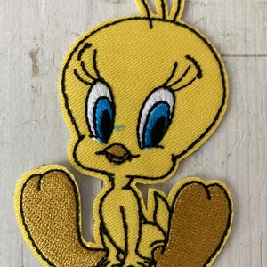 Op de afbeelding: Gele Tweety Bird-patch met zwarte omtrek. Het stripfiguur heeft grote blauwe ogen, een gele snavel en bruine voeten. De patch is gemaakt van stof en is geschikt voor kleding of accessoires.