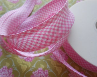 Könnte beinhalten: Rosa-weißes Gingham-Band auf einer Spule. Das Band ist gefaltet und verdreht, wodurch das Muster sichtbar wird.