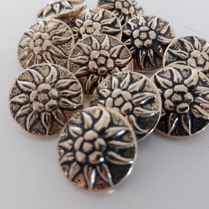 May include: A selection of bronze-coloured metal buttons. Each button showcases a detailed floral design with a central flower and surrounding petals. The buttons are round and have a slightly raised relief.