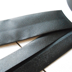 May include: Close-up of black leather strips with a textured surface. The strips are curved and appear to be part of a larger item. The image is well-lit, highlighting the details of the material.