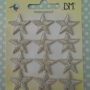 Pode incluir: Um pacote de 12 patches termocolantes em forma de estrela prateada. O pacote é etiquetado com "Termoadesivi" e "BM".