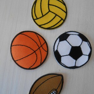 Può includere: Quattro toppe ricamate con diversi palloni da sport: una pallavolo gialla, una pallacanestro arancione, un pallone da calcio bianco e nero e un pallone da football americano marrone.