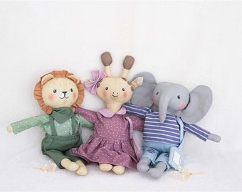 May include: Three plush stuffed animals: a lion wearing green overalls, a giraffe wearing a pink polka dot dress, and an elephant wearing a blue and white striped shirt and blue jeans.