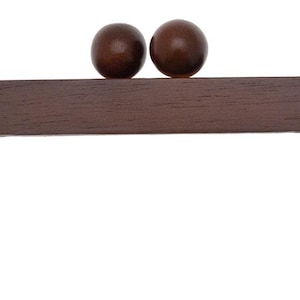 May include: A dark brown wooden purse frame with two round, dark brown wooden ball clasps. The frame has a rectangular shape with rounded corners and is designed for bag making.