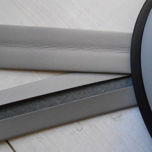 May include: Close-up of gray upholstery trim with a black backing. The trim is folded in half, showing the black backing.