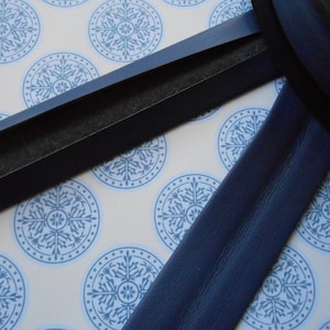 May include: Two black fabric trims, one with a fuzzy backing, on a white background with blue snowflake patterns.