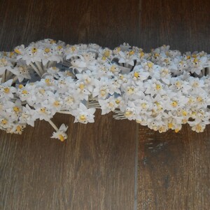 May include: A cluster of white artificial flowers with yellow centres, arranged in a row. The flowers are attached to thin wires and are likely for crafting or decorating.