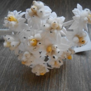 May include: A bunch of white felt flowers with yellow centres. The flowers are arranged in a bouquet and have a rustic, vintage feel.