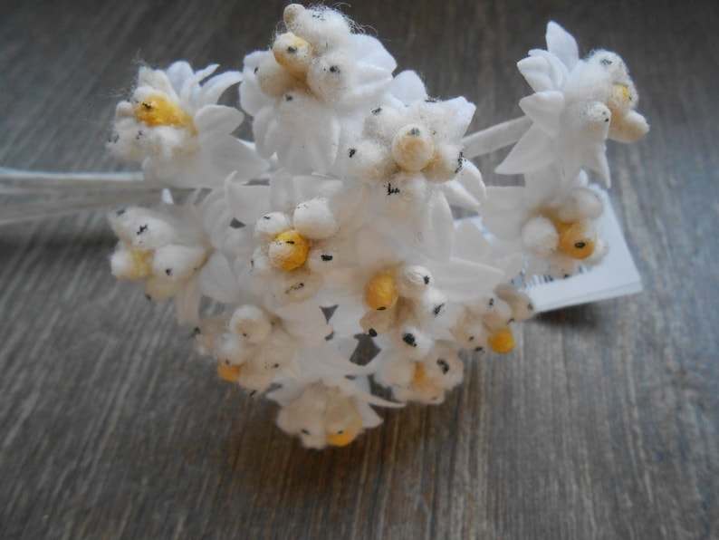 May include: A bunch of white felt flowers with yellow centres. The flowers are arranged in a bouquet and have a rustic, vintage feel.