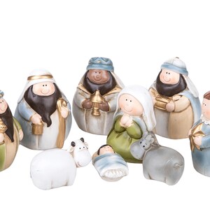 Könnte beinhalten: Ein Krippenset mit neun abgerundeten Figuren, darunter Personen in grünen, blauen und beigen Gewändern, ein weißes Schaf, ein grauer Esel und ein gewickeltes Kind. Die Figuren haben bemalte Gesichter, goldene Akzente und Kopfbedeckungen.