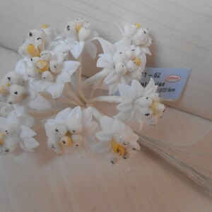 May include: A bunch of white felt flowers with yellow centres and black accents. The flowers are attached to thin wire stems. The flowers are approximately 6.5 cm in diameter.