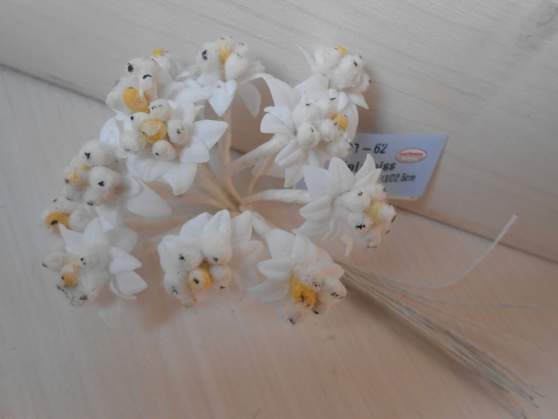May include: A bunch of white felt flowers with yellow centres and black accents. The flowers are attached to thin wire stems. The flowers are approximately 6.5 cm in diameter.