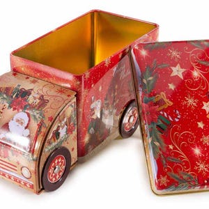 Könnte beinhalten: Eine weihnachtliche Blechdose in Form eines Oldtimer-Lastwagens. Die Dose ist mit Illustrationen von Weihnachtsmann, Rentieren und festlichen Dekorationen verziert. Der Deckel ist geöffnet und gibt einen goldenen Innenraum frei. Die Dose ist rot, gold und braun.