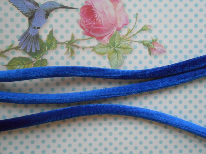 May include: Three strands of royal blue velvet cord, each about 1/2 inch wide, are laid out on a white background with blue polka dots.