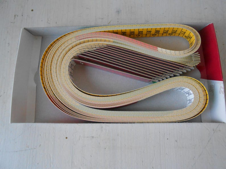 May include: A collection of measuring tapes and cards in a white box with a red accent. The tapes are yellow with black markings, and the cards are red and white. The tapes are curled in a loop.