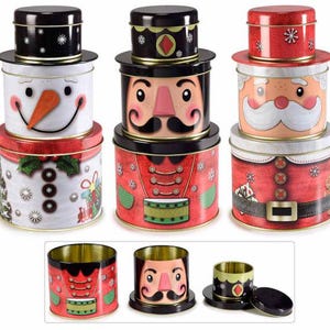 May include: A collection of three Christmas-themed tins. The tins are decorated with snowman, nutcracker, and Santa Claus designs. Each tin has a matching lid. The snowman tin has a carrot nose and a smiling face. The nutcracker tin has a mustache. The Santa tin has a white beard.
