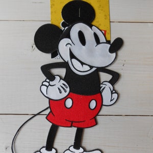 Peut inclure: Patch thermocollant brodé en noir et blanc de Mickey Mouse avec un short rouge. Le patch est sur un fond jaune avec une icône de fer blanc.