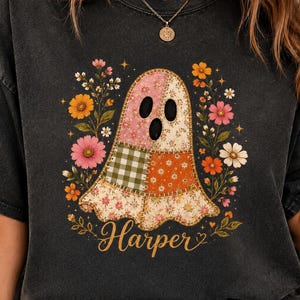 May include: A charcoal grey t-shirt featuring a central graphic of a ghost made of various floral and checkered fabric patches. The ghost is surrounded by colourful wildflowers and the name Harper is printed in a gold script font below the ghost.