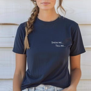 May include: Navy blue t-shirt with the text "Show me... Tell me..." printed in white. The shirt has short sleeves and a crew neck. The fabric appears soft and comfortable.
