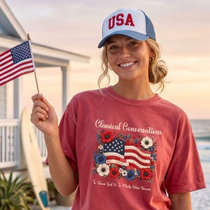May include: A red t-shirt with the text "Classical Conversations" and an American flag design with flowers. A white and blue "USA" hat is worn. An American flag is held in the hand.