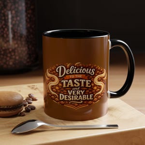 May include: A brown coffee mug with a black handle and interior. The mug features the text "Delicious to the Taste and Very Desirable" in an ornate design. A spoon and a macaron are in the foreground.