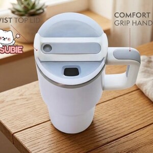 A white and gray insulated travel mug with a twist-top lid and a comfortable grip handle, placed on a wooden table.