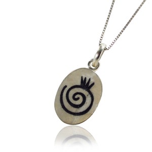 May include: A silver chain necklace with an oval pendant featuring a black spiral design and a small crown on top.
