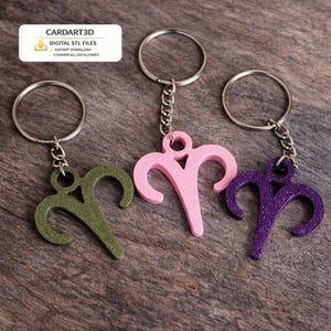May include: Three keychains in olive green, pink, and purple, each featuring an Aries zodiac symbol. The keychains are attached to silver key rings and chains. The background is a wooden surface. The image includes text that says "CARDART3D" and "DIGITAL STL FILES".