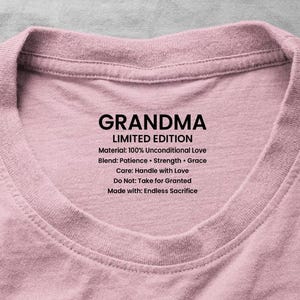 Op de afbeelding: Een lichtroze t-shirt met het woord "GRANDMA" in vette zwarte letters. Daaronder staat de tekst "LIMITED EDITION" en een lijst met kwaliteiten: "Geduld, Kracht, Genade". Het materiaal wordt beschreven als "100% Onvoorwaardelijke Liefde."