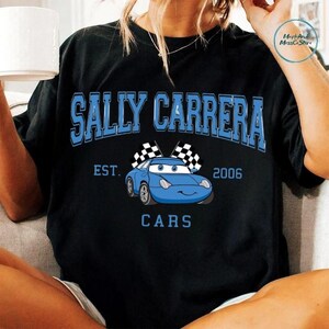 A person wearing a black t-shirt with a graphic design featuring a blue car and the text "Sally Carrera" and "Cars" printed on it.