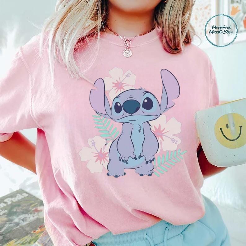 A person wearing a pink t-shirt with a cartoon character printed on it, holding a coffee mug with a smiley face on it.