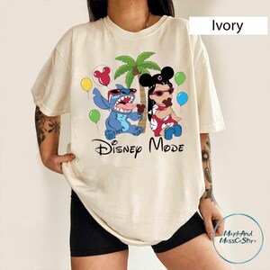 A person wearing a white t-shirt with a Disney-themed graphic design featuring characters from the Disney movie "Stitch" and the text "Disney Mode".